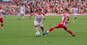 Multiple men playing football in a filled stadium with people